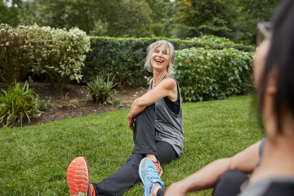Mujer sonriente realizando estiramientos al aire libre en un parque, destacando los beneficios del ejercicio para la salud mental.