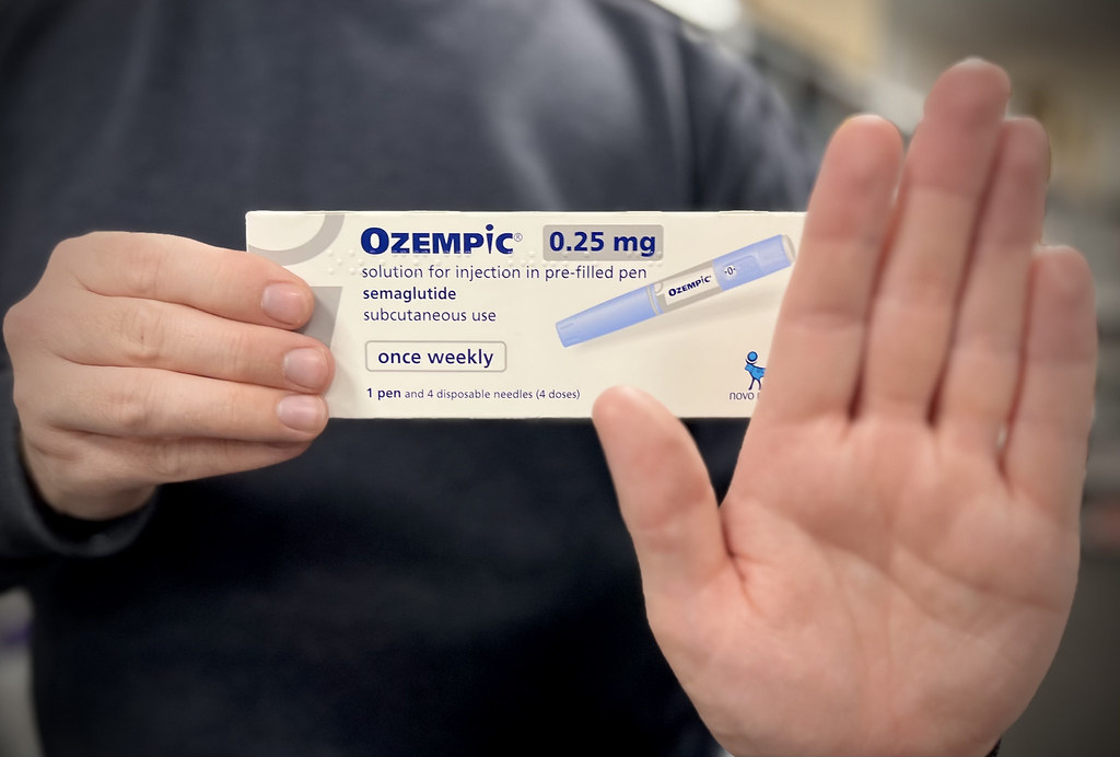 Caja de Ozempic 0.25 mg con pluma inyectable de semaglutida para uso subcutáneo semanal, mostrando información del medicamento y logo de Novo, sostenida por mano con jersey negro sobre fondo desenfocado
